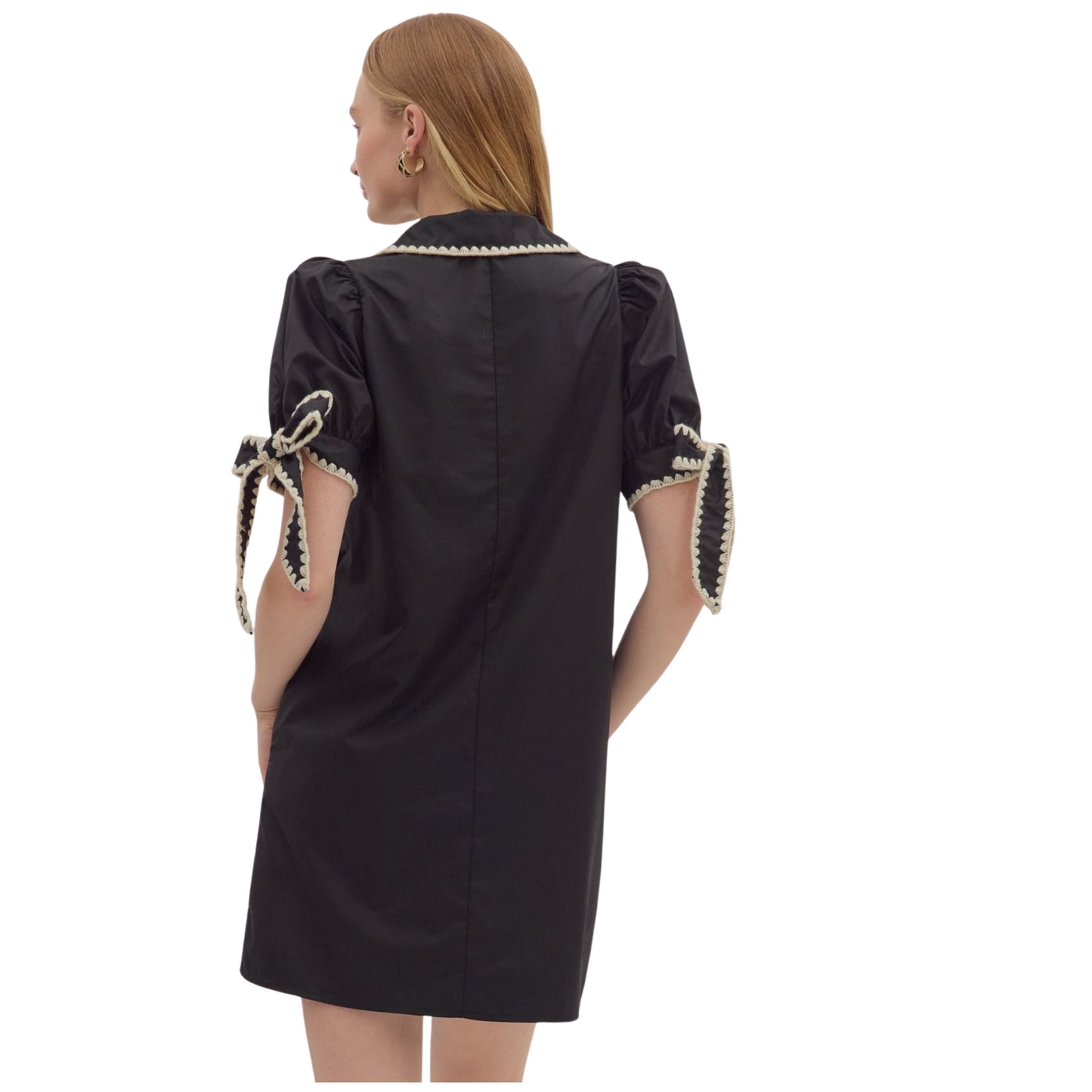 This lightweight woven mini dress features short puff sleeves and a structured collar with a V-neck detailed by contrasting scallop binding. Designed with tie cuffs and practical side pockets, it combines style with function. Fully lined and non-sheer, it offers comfort and coverage in a sleek black hue, ideal for versatile seasonal wear.