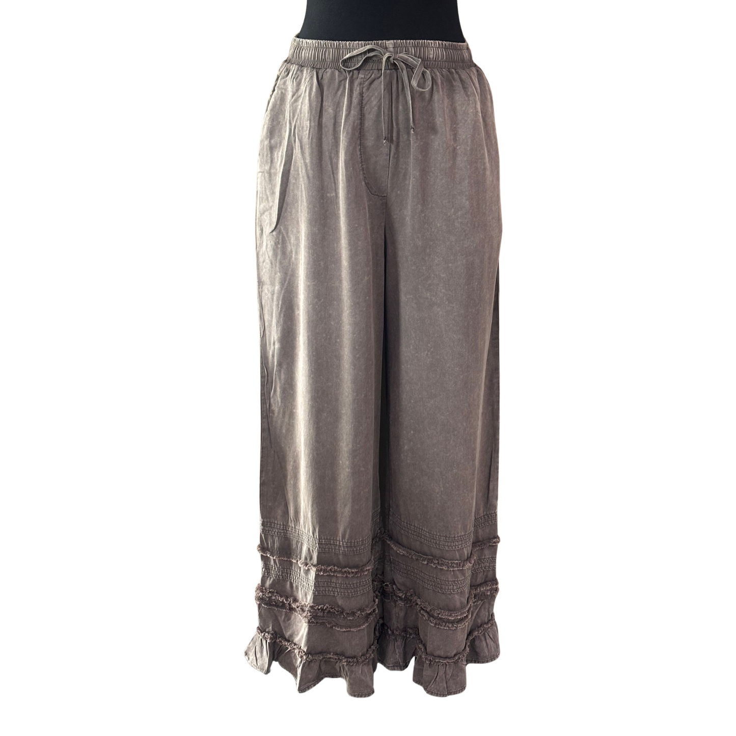 Charcoal ruffle pants by Blue Velvet featuring a comfortable elastic waistband with adjustable drawstring. The playful ruffle detailing adds movement and style to your everyday wardrobe. Perfect for casual wear, lounging, or dressing up with the right top. The drawstring allows for a customized fit, while the elastic waist ensures all-day comfort. A versatile piece that transitions seamlessly from day to night.