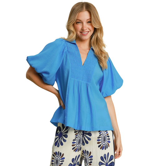 Expertly designed by Umgee, this Bubble Sleeve Smocked Top is a must-have piece for your wardrobe. The blue color adds a touch of sophistication while the smocked detail and exaggerated bubble sleeve create a trendy and flattering silhouette. Perfect for any occasion with its classic v neck design.