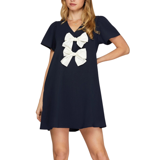 Elevate your wardrobe with this charming She+Sky mini dress, designed for effortless style. The navy woven fabric provides a classic foundation, while delicate white bow accents add a playful, feminine touch. The flattering V-neckline creates a sophisticated silhouette perfect for any occasion—from casual outings to evening events. Lightweight and versatile, this dress pairs beautifully with sneakers for a relaxed look or heels for something more polished. 