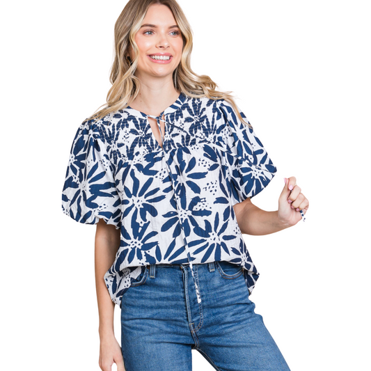 This Floral Smocked Tie Top features a charming flower print and a stylish self-tie neck. The smocked yoke adds a touch of texture, and the short puffed sleeves provide a feminine touch. Made of lightweight, non-sheer navy fabric, this top is perfect for any occasion.