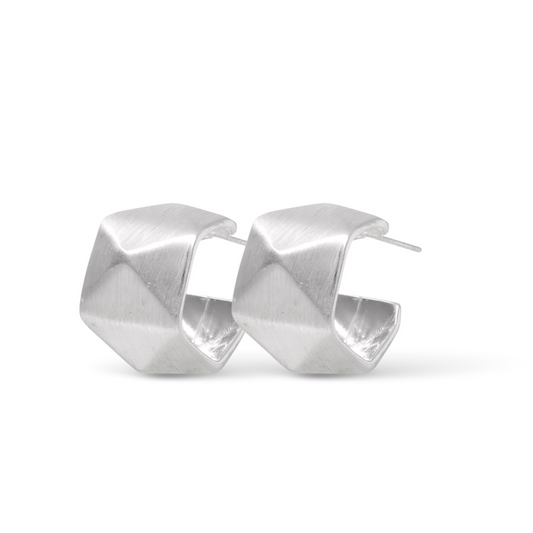 Crafted with a bold yet delicate silver finish, the Hanna Facet Wide Huggie Earrings feature a modern and abstract design. These small hoops are perfect for any occasion, adding a touch of style and elegance to your look. With a matte finish, these earrings are both versatile and eye-catching.