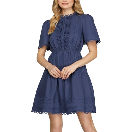 Navy woven mini dress by She+Sky featuring a classic round neckline and delicate lace detailing. Short sleeves provide comfortable everyday wear, while the tiered silhouette adds dimension and movement. Functional pockets keep essentials close. Perfect for casual outings or dressed up for evening occasions.