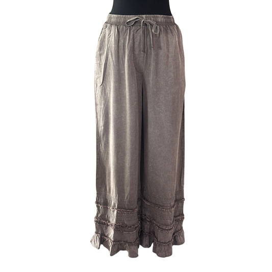 Charcoal ruffle pants by Blue Velvet featuring a comfortable elastic waistband with adjustable drawstring. The playful ruffle detailing adds movement and style to your everyday wardrobe. Perfect for casual wear, lounging, or dressing up with the right top. The drawstring allows for a customized fit, while the elastic waist ensures all-day comfort. A versatile piece that transitions seamlessly from day to night.