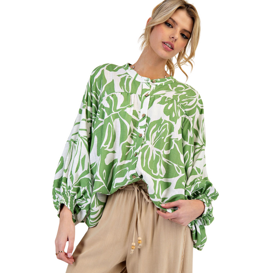 This printed rayon linen button-down shirt features long dolman sleeves with smocked cuffs and a notched neckline for a refined silhouette. The rounded hem and ruched detailing on the chest and back add subtle texture and dimension. Crafted with a relaxed, loose fit and adorned with an elegant leaf print, this shirt combines comfort with sophisticated style, making it a versatile addition to any wardrobe.