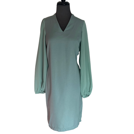 This GiGio mini dress in a sophisticated sage hue features a flattering V-neckline and sheer long sleeves that add an elegant touch. Designed with a back slit and keyhole details, it combines subtle allure with refined style, making it an excellent choice for both day and evening occasions.