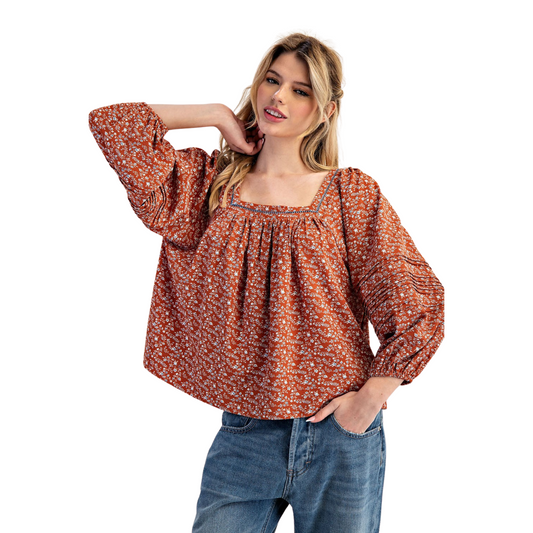 This elegant long-sleeve blouse features a flattering square neckline and a delicate floral print set against a warm clay color. Designed for a refined silhouette, it combines classic charm with modern sophistication, making it ideal for both professional settings and casual occasions. The breathable fabric ensures comfort throughout the day while the subtle floral pattern adds a touch of understated femininity.