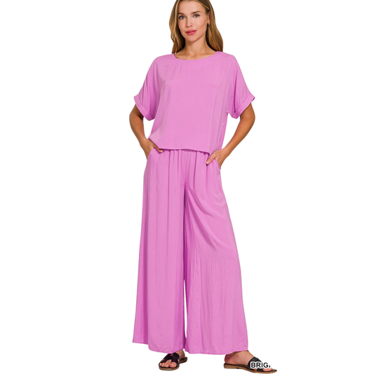 Elevate your casual wardrobe with this thoughtfully designed Zenana outfit set. Featuring a vibrant bright mauve short-sleeve top paired with coordinating long pants, this two-piece ensemble delivers effortless style and versatility. The woven fabric construction ensures breathability and comfort throughout the day, while the coordinated color palette simplifies mixing and matching. Perfect for layering or wearing as a complete look, this set transitions seamlessly from weekend errands to relaxed social gat